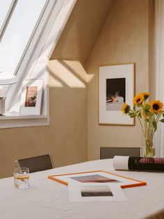 a white table topped with a vase filled with yellow flowers next to a framed photo