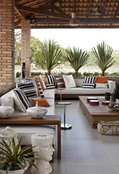 a living room filled with lots of furniture under a wooden roof covered in palm trees