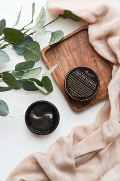 the body scrub is next to some green leaves and a wooden tray with an inscription on it