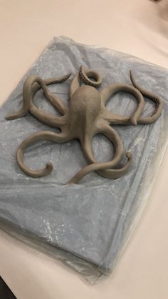 an octopus sculpture sitting on top of a sheet of plastic next to a white table