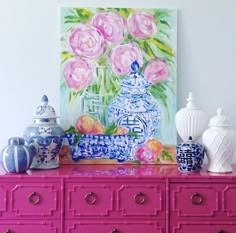 a pink dresser with blue and white vases on it's top, next to a painting