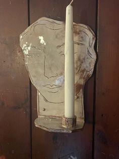 a candle that is sitting in front of a glass face on a wooden wall with wood paneling