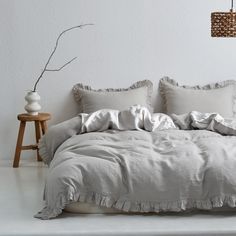 an unmade bed with white linens and ruffled edges in a minimalist bedroom