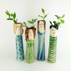 three small vases with plants in them on a white surface, one is made to look like people