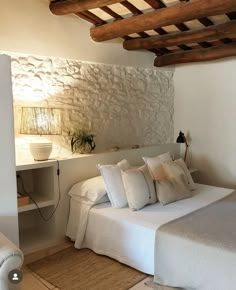 a white bed sitting in a bedroom next to a wall mounted lamp and wooden beams