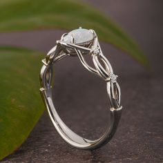 a white gold ring with an opal and diamond set in the center, on top of a green leaf