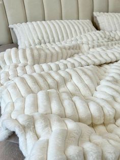 the bed is made up with white furs and pillows on top of each other