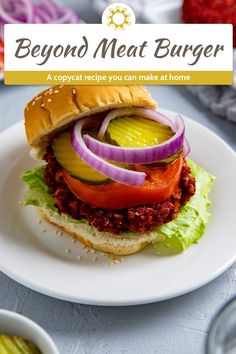 a burger with onions, tomato and lettuce on it sitting on a white plate