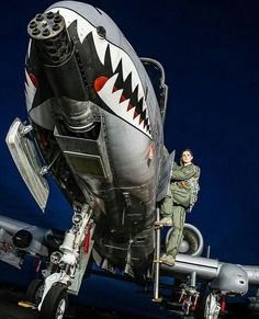 a fighter jet with a shark face painted on it's side and pilot standing next to it