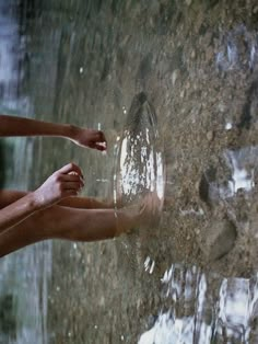 a woman's legs are reflected in the water on a stone wall, while her hand is reaching for something