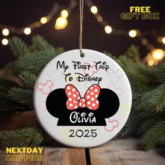 a christmas ornament hanging from a tree with lights in the background and text that reads, my first trip to disney