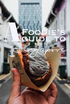 a person holding up a piece of food in the middle of a street with buildings behind them