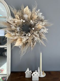 a christmas wreath on top of a wooden table next to a candle and small white houses