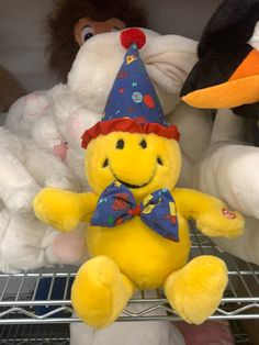 a yellow stuffed animal with a party hat and bow tie sitting on a shelf in a store