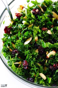 a glass bowl filled with greens and cranberry toppings on top of a white table