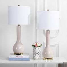 two lamps on a table next to a vase with flowers and books in front of it