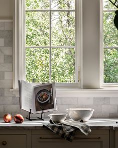 an open book sitting on top of a kitchen counter next to two bowls and apples