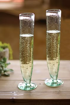 two champagne flutes sitting on top of a wooden table next to each other with bubbles in them