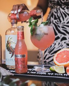 a person pouring a drink into a glass next to grapefruit and limes