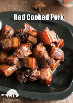 a black plate topped with cooked pork on top of a wooden table