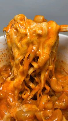 a spoon full of macaroni and cheese being lifted from a bowl with chopsticks