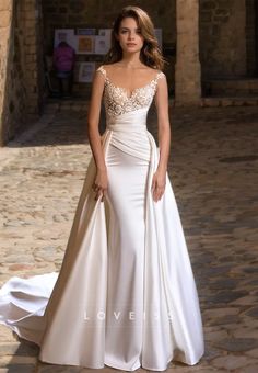 a woman in a white wedding dress standing on a cobblestone street with her hand on her hip