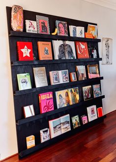 a book shelf filled with lots of books on top of a hard wood floor next to a white wall