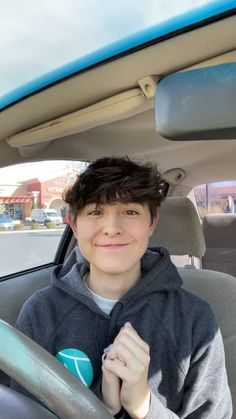 a boy sitting in the passenger seat of a car with his hand on the steering wheel