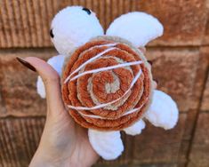 a hand holding a small stuffed animal with white yarn on it's face and brown hair