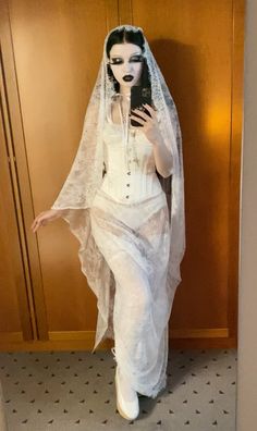 a woman dressed in white is taking a selfie with her cell phone while wearing a veil