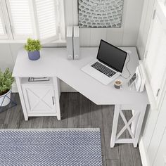 a laptop computer sitting on top of a white desk next to a potted plant