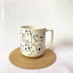 a coffee cup with cats drawn on it sitting on top of a place mat in front of a white wall