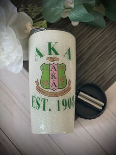 a white can with green and pink crest on it sitting next to a flower pot