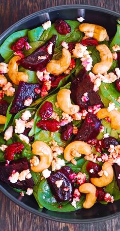 a salad with beets, nuts and spinach leaves in a black bowl on a wooden table