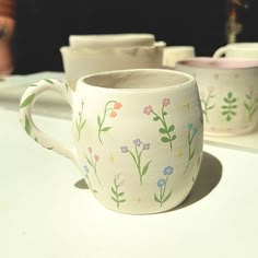 two coffee mugs sitting on top of a counter next to each other with flowers painted on them