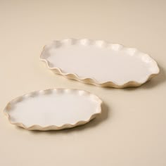 two white scalloped dishes sitting on top of a table next to each other