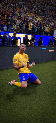 a soccer player sitting on the ground in front of a crowd at a stadium with his mouth open