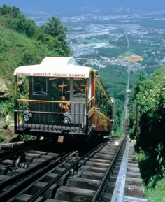 a trolley car is going down the tracks near some trees and mountains in the background