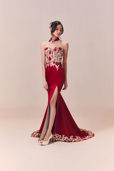 a woman in a long red dress with gold embroidery on the side and high slit