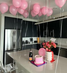 pink balloons are hanging from the ceiling above a kitchen counter with a cake and wine bottle