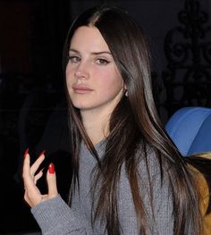 a woman with long brown hair and red nails holding a cell phone in her hand