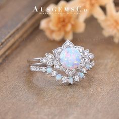 an opal and diamond ring sits on top of a wooden table next to flowers