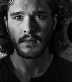 a black and white photo of a man with long curly hair looking at the camera