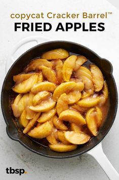 a frying pan filled with fried apples on top of a white counter next to a spoon