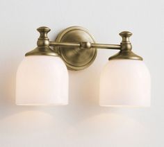 two light bathroom fixture with frosted glass shades on the top and bottom lights in an antique brass finish