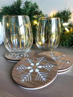 three wine glasses sitting on top of a wooden table next to christmas tree branches and lights