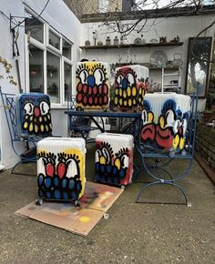 four colorfully painted suitcases sitting on top of a metal stand in front of a building