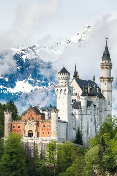 an old castle in the mountains with snow on it's top and trees below