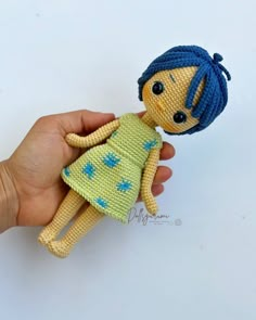 a hand holding a small doll with blue hair on it's head and wearing a green dress