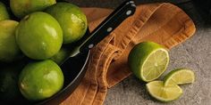 limes are in a bowl on a table with a knife next to them and a wooden cutting board